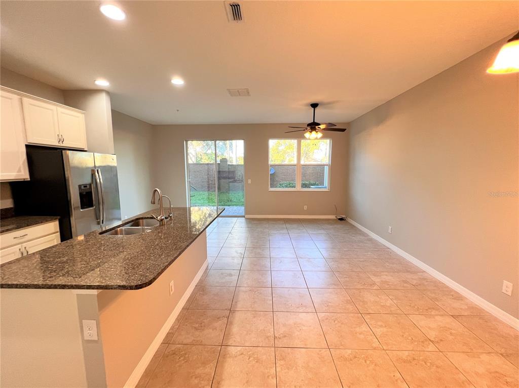 A kitchen with granite countertops and a stainless steel refrigerator opens to a tiled living area — 1123 PALMA VERDE PLACE, APOPKA, FL