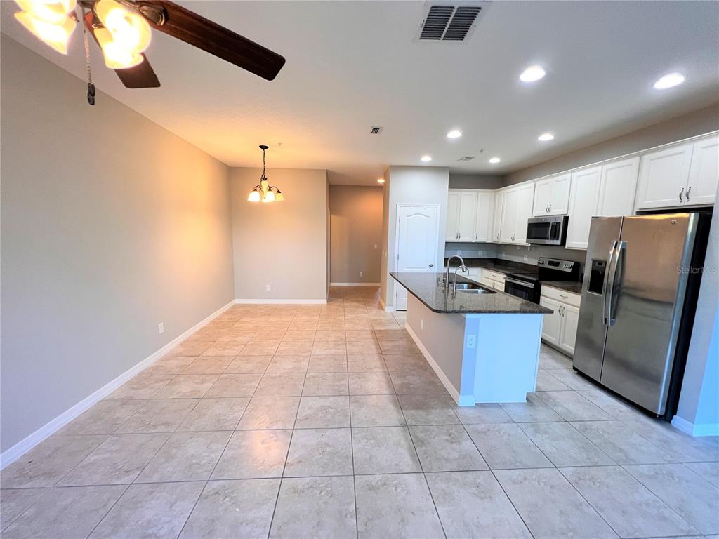 A kitchen and dining area feature white cabinets, stainless steel appliances, and tiled flooring — 1123 PALMA VERDE PLACE, APOPKA, FL
