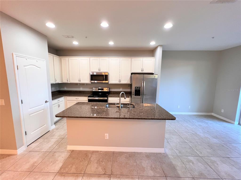 A kitchen features white cabinets, granite countertops, a center island, and stainless steel appliances — 1123 PALMA VERDE PLACE, APOPKA, FL