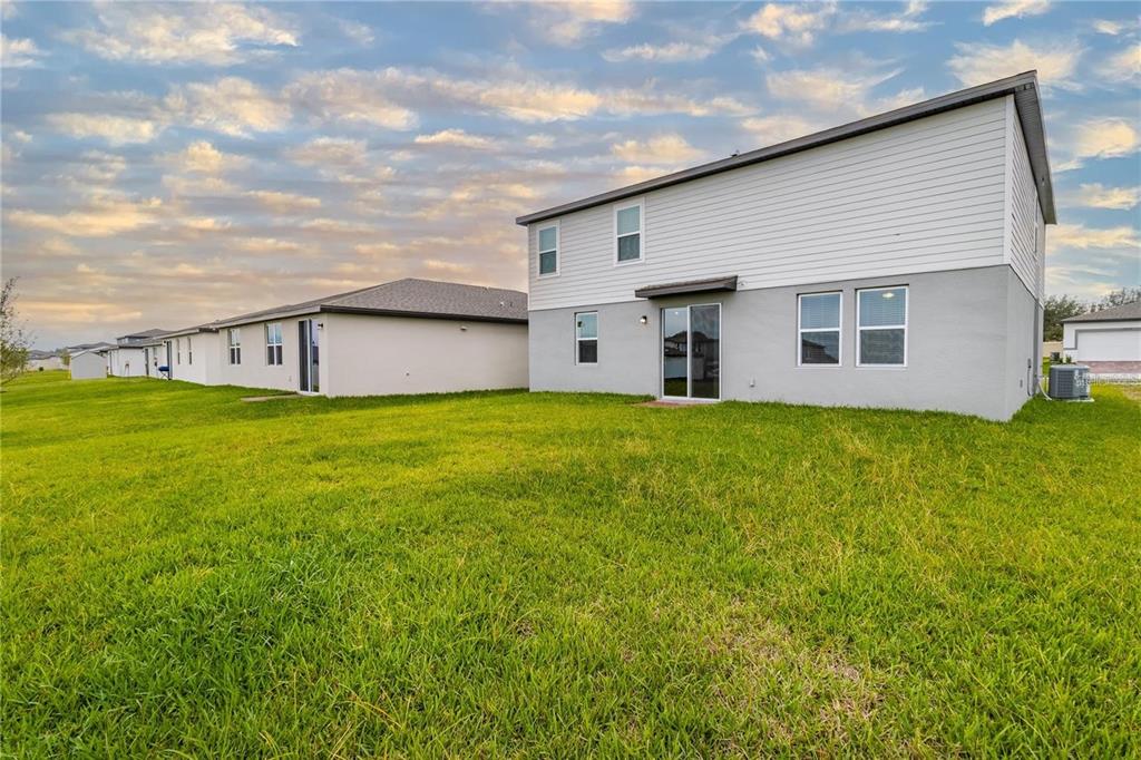 The back exterior of a two-story house with a large grassy yard — 3033 CASSIDY LANE, HAINES CITY, FL