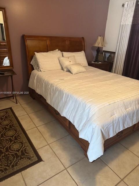 A bedroom features a wooden bed frame, white bedding, and tile flooring — 4299 NW 16th St # 103, Lauderhill FL 33313, LAUDERHILL, FL