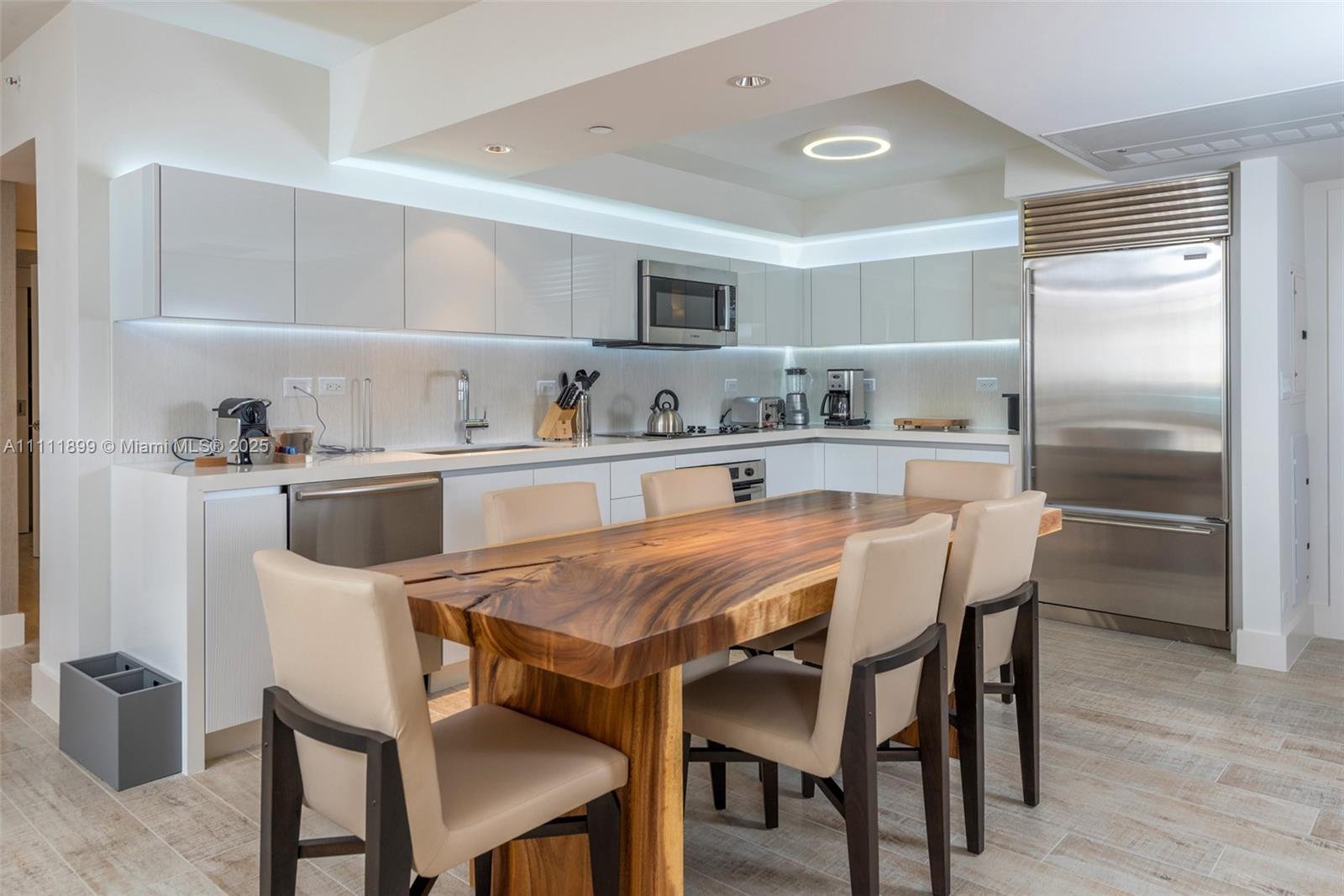 A modern kitchen features white cabinetry, stainless steel appliances, and a large live-edge wood table — 102 24th St # 1015, Miami Beach FL 33139, MIAMI BEACH, FL
