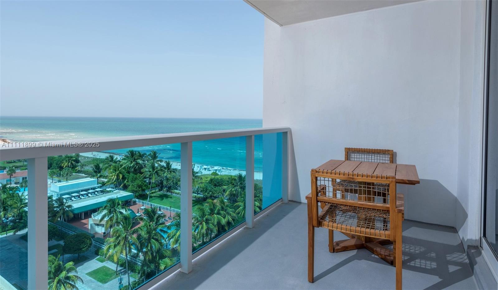 A balcony with a wooden table and chairs overlooks the ocean and palm trees — 102 24th St # 1015, Miami Beach FL 33139, MIAMI BEACH, FL