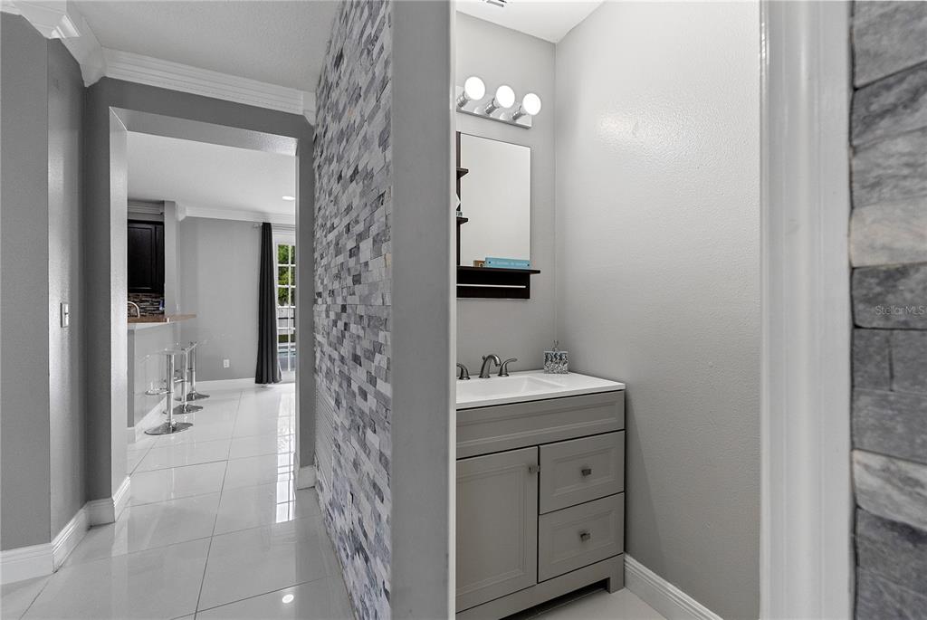 A gray vanity with a sink sits in a bathroom featuring a stone-tiled accent wall — 963 SPRINGS LANDING DRIVE, DELTONA, FL