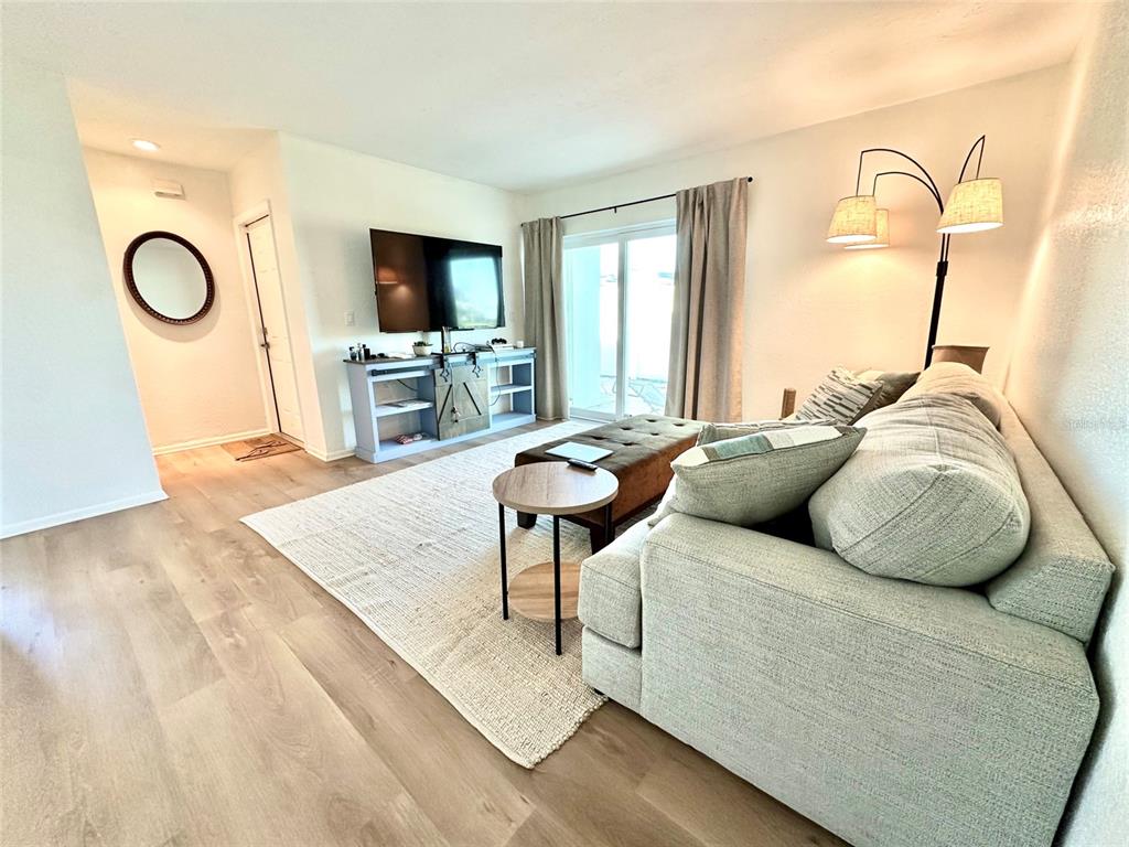 A living room features light wood flooring, a gray sofa, a television, and sliding glass doors — 5771 GALLATIN LANE, NORTH PORT, FL