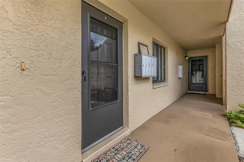 A covered exterior walkway features two dark-framed doors, a wall-mounted mailbox, and a welcome mat — 4000 OAKVIEW DRIVE UNIT L4, PORT CHARLOTTE, FL