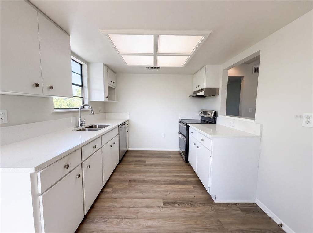 A galley kitchen features white cabinets, white countertops, stainless steel appliances, and wood-look flooring — 516 42ND STREET COURT W, PALMETTO, FL