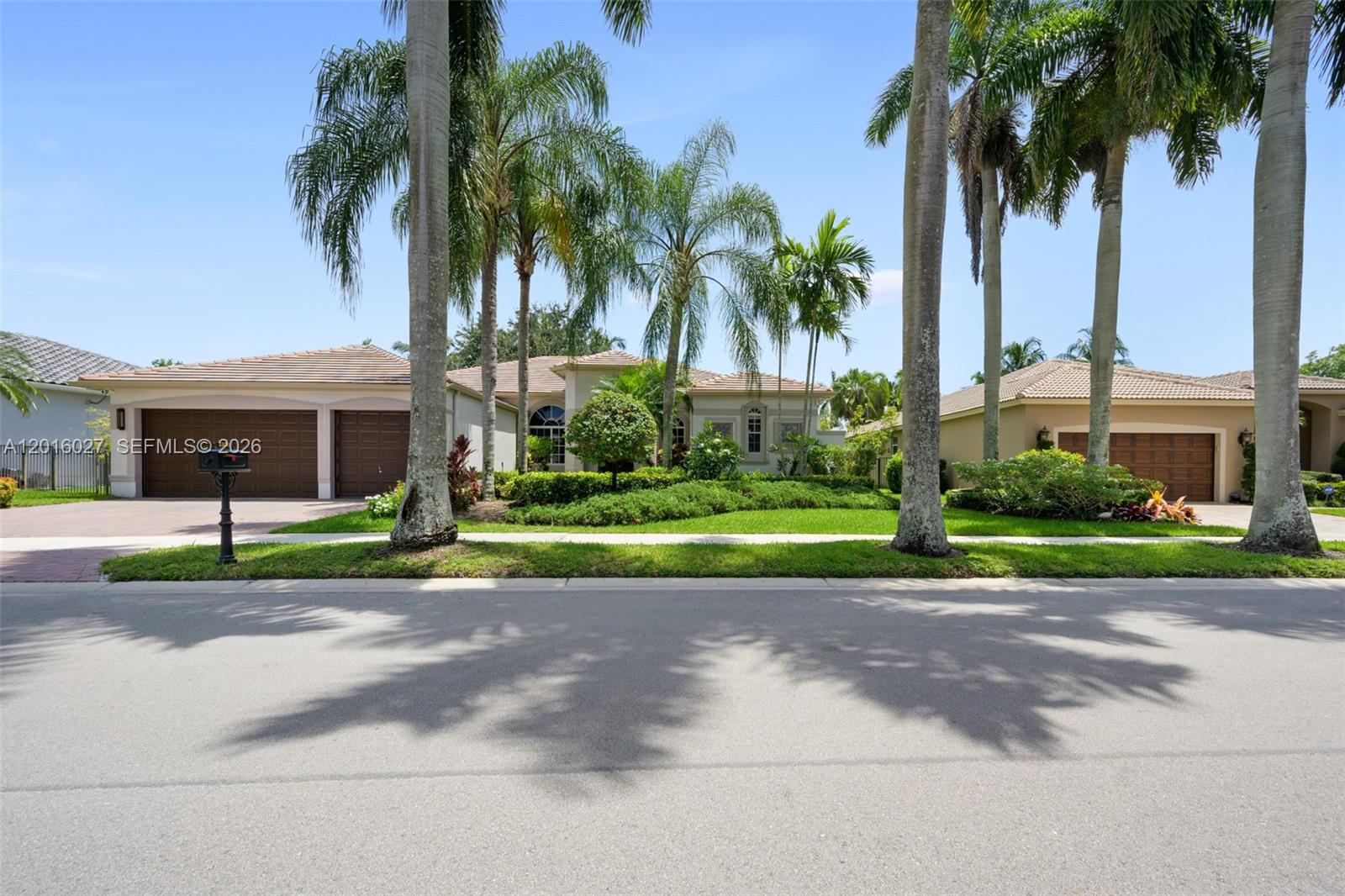 A street-level view of a single-story house with a garage and palm trees — 2538 Eagle Run Dr, Weston FL 33327, WESTON, FL
