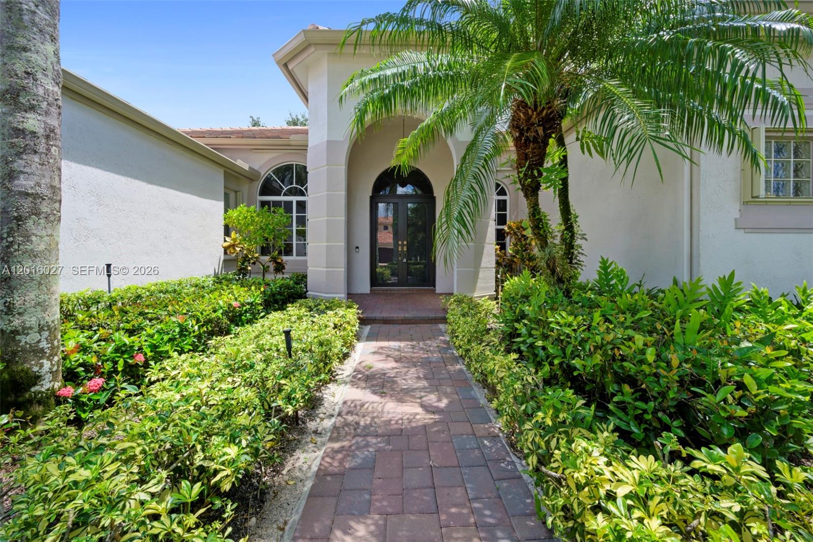 A brick walkway leads to the arched front entrance of a house with lush landscaping — 2538 Eagle Run Dr, Weston FL 33327, WESTON, FL