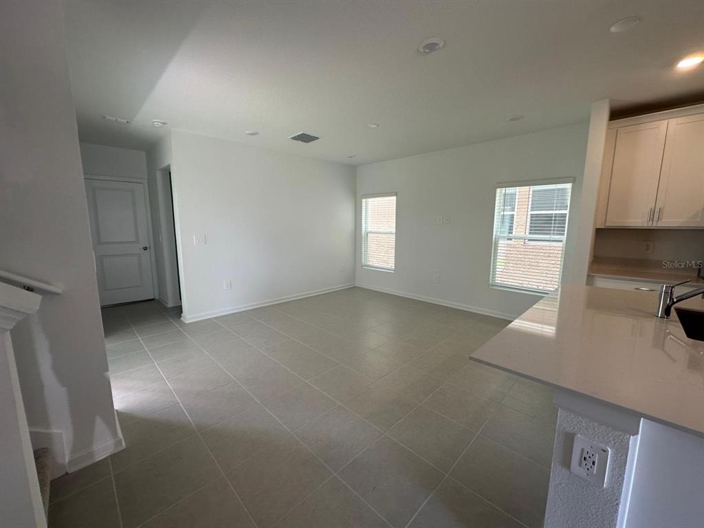 An open-concept living area features light tile flooring, white walls, and a kitchen island — 2895 TRANSFORMATION WAY, CLERMONT, FL