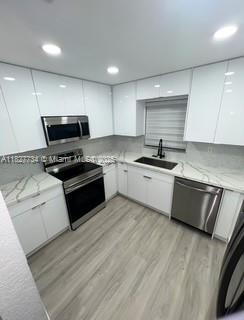 A modern kitchen features white cabinets, stainless steel appliances, and light wood-look flooring — 964 N 18th Ct, Hollywood FL 33020, HOLLYWOOD, FL