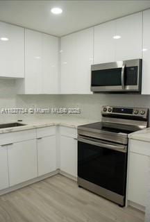 A modern kitchen features white flat-panel cabinets, stainless steel appliances, and light wood-look flooring — 964 N 18th Ct, Hollywood FL 33020, HOLLYWOOD, FL