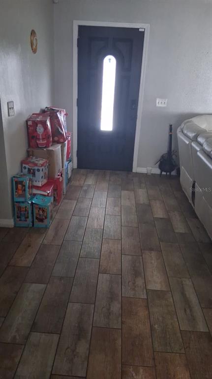 A front entryway features wood-look tile flooring, a dark door, and a stack of boxes — 8016 APACHE LANE, LAKELAND, FL