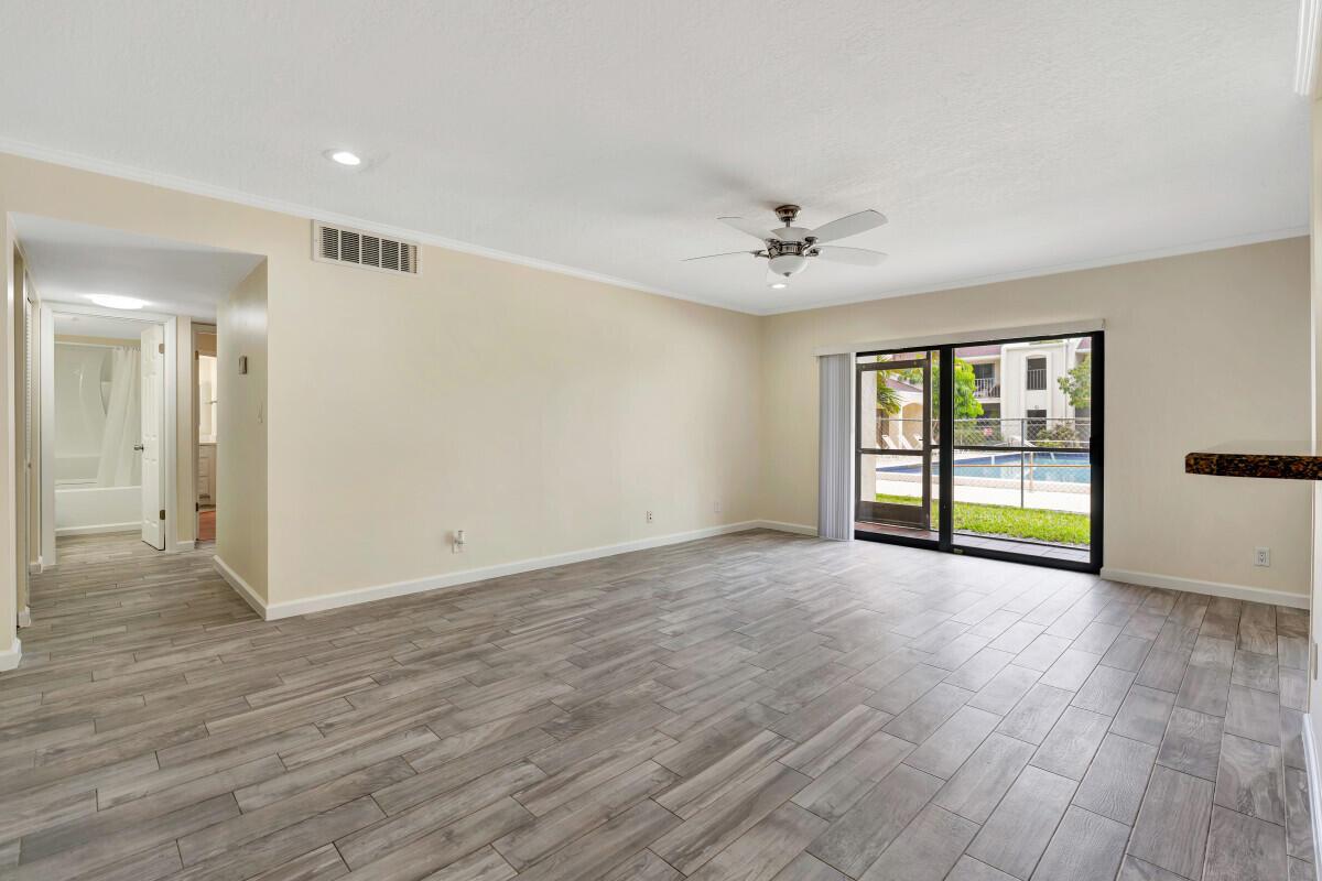 An empty living room with wood-look tile flooring, a ceiling fan, and sliding glass doors — 150 Pineview Road # F3, Jupiter FL 33469, JUPITER, FL