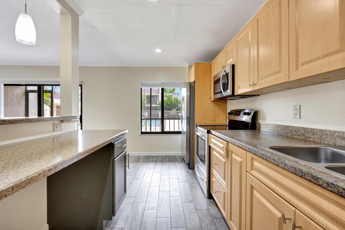 A kitchen features light wood cabinets, granite countertops, stainless steel appliances, and gray wood-look flooring — 150 Pineview Road # F3, Jupiter FL 33469, JUPITER, FL