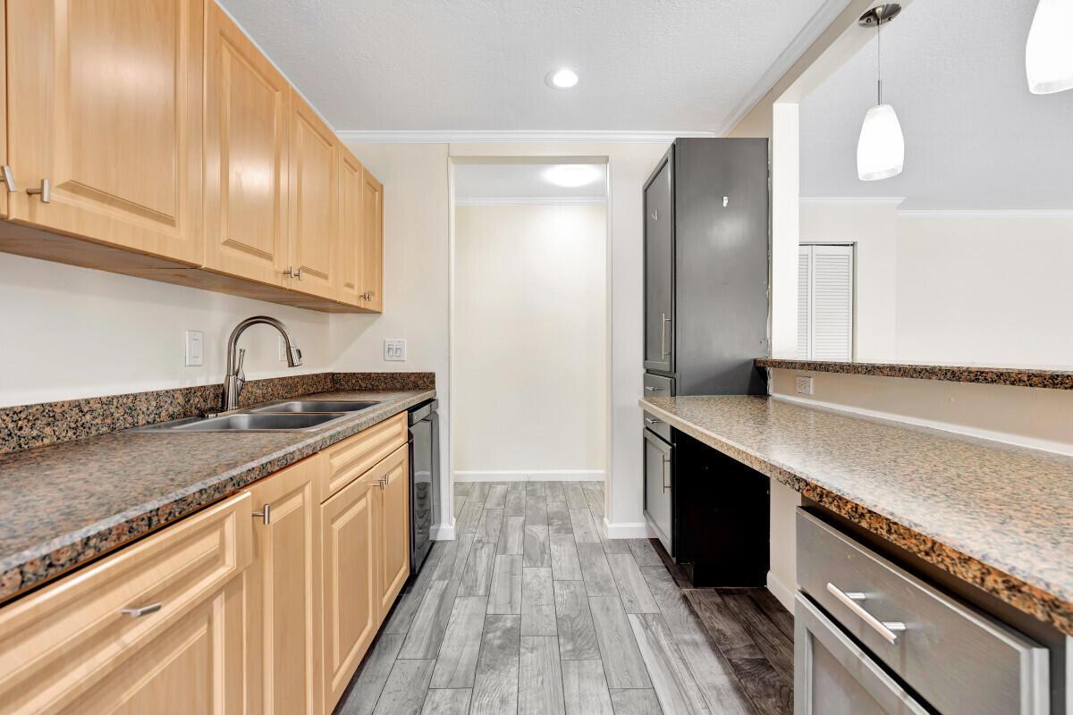A kitchen features light wood cabinets, granite countertops, stainless steel appliances, and gray wood-look flooring — 150 Pineview Road # F3, Jupiter FL 33469, JUPITER, FL
