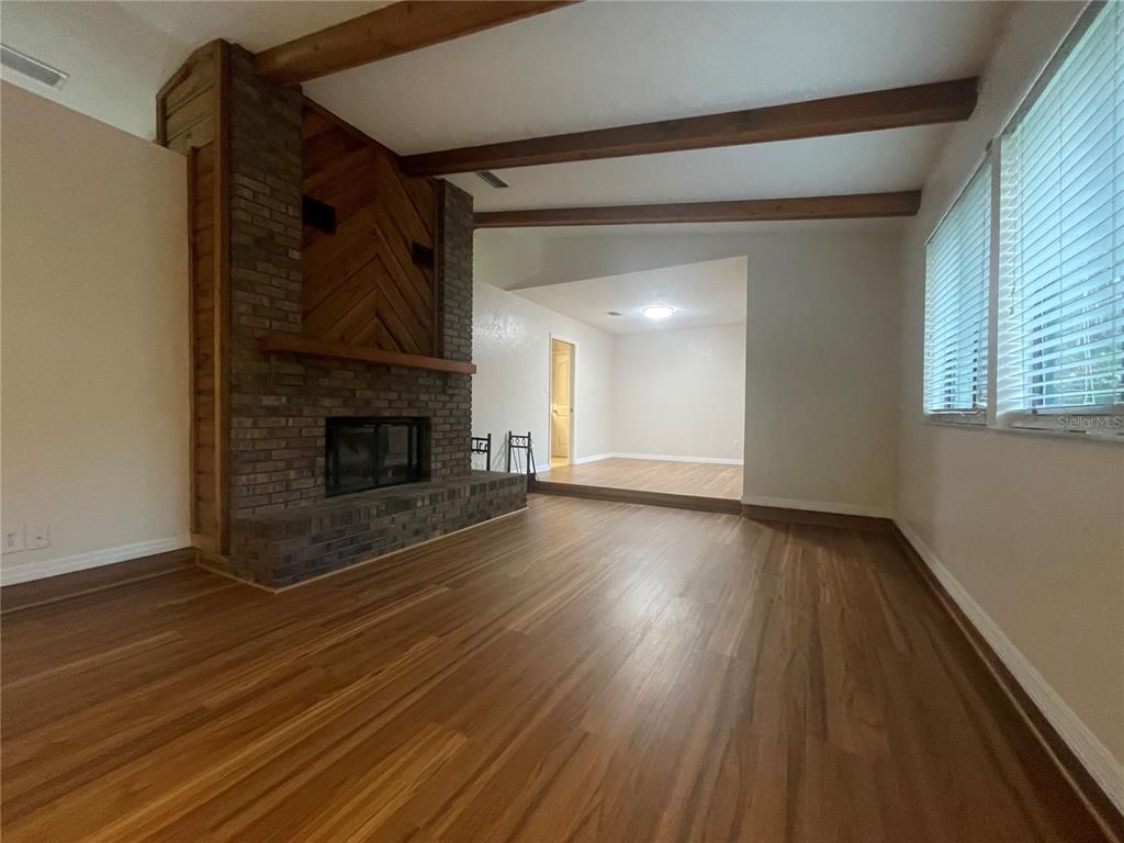 A living room features a brick fireplace, exposed wood ceiling beams, and wood-look flooring — 3810 NW 28TH TERRACE, GAINESVILLE, FL