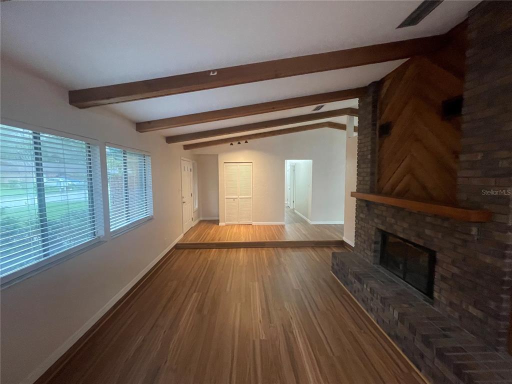 A living room features wood-look flooring, exposed ceiling beams, and a brick fireplace — 3810 NW 28TH TERRACE, GAINESVILLE, FL