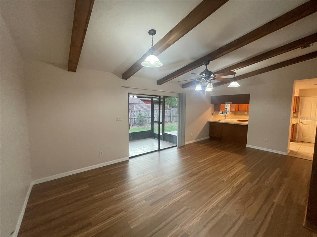 A living room with wood-look flooring, exposed ceiling beams, and a sliding glass door — 3810 NW 28TH TERRACE, GAINESVILLE, FL