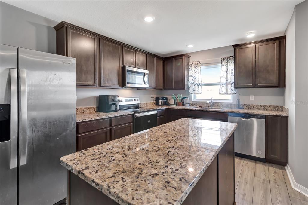 A kitchen features dark wood cabinets, granite countertops, stainless steel appliances, and a central island — 1691 WYNFORD CIRCLE, TAVARES, FL