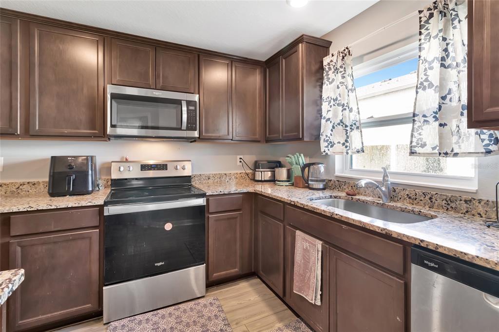 A kitchen features dark wood cabinets, granite countertops, stainless steel appliances, and a window — 1691 WYNFORD CIRCLE, TAVARES, FL