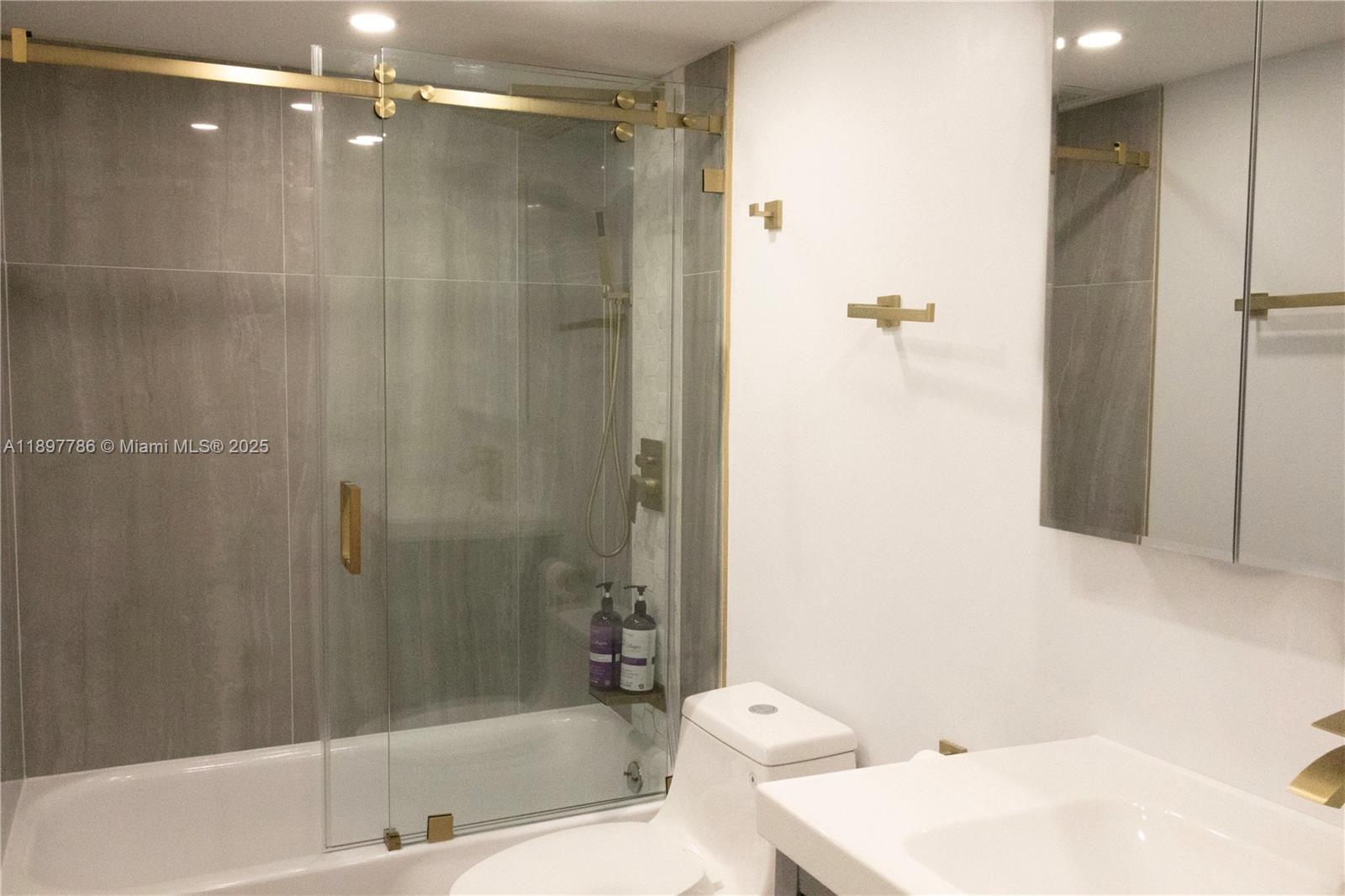 A bathroom features a glass-enclosed shower with gold hardware, a white toilet, and a vanity — 5005 Collins Ave # 1523, Miami Beach FL 33140, MIAMI BEACH, FL