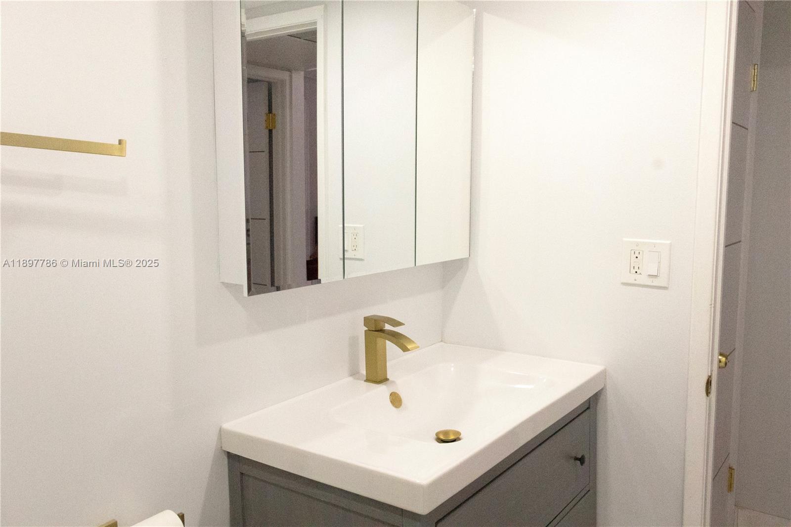 A bathroom features a gray vanity, white sink, gold faucet, and a mirrored medicine cabinet — 5005 Collins Ave # 1523, Miami Beach FL 33140, MIAMI BEACH, FL