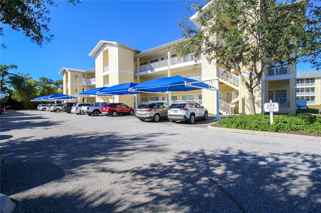 A multi-story apartment building with covered parking spaces and a landscaped area in front — 101 NATURES WAY UNIT 1202, ROTONDA WEST, FL