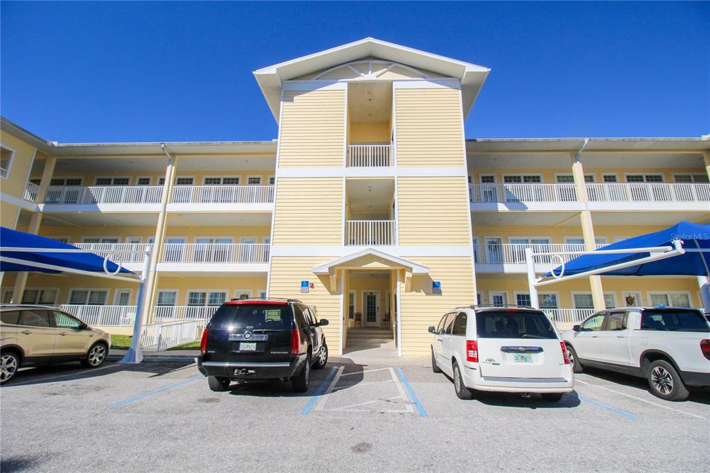 A three-story yellow building with balconies and a parking lot in the foreground — 101 NATURES WAY UNIT 1202, ROTONDA WEST, FL