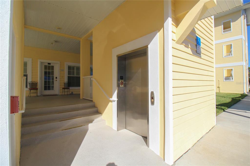 An exterior view of a yellow building featuring a covered entrance, stairs, and an elevator — 101 NATURES WAY UNIT 1202, ROTONDA WEST, FL