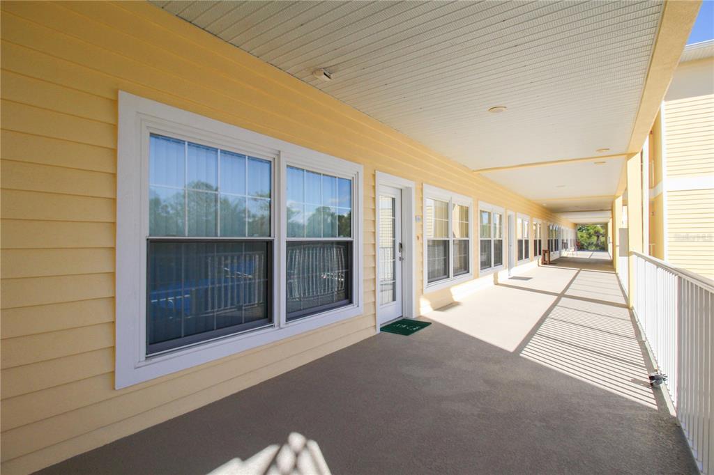 A long, covered outdoor walkway with yellow siding, multiple windows, and a white railing — 101 NATURES WAY UNIT 1202, ROTONDA WEST, FL
