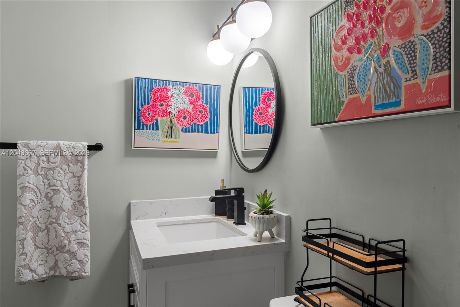 A small bathroom features a white vanity, black fixtures, a round mirror, and floral artwork — MIAMI, FL