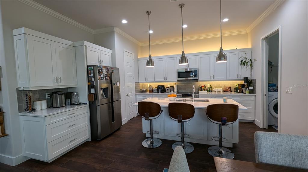 A modern kitchen features white cabinetry, a central island with bar stools, and stainless appliances — 7476 SW 66TH LANE, GAINESVILLE, FL