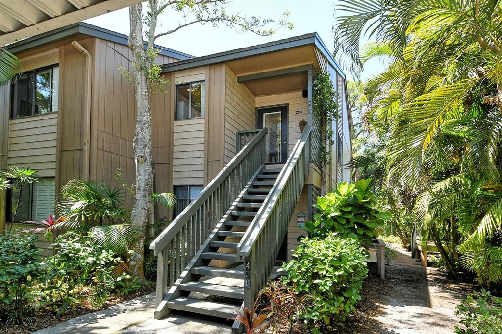 An exterior view of a two-story tan building with wooden stairs leading to an entrance — 1720 GLENHOUSE DRIVE UNIT GL430, SARASOTA, FL