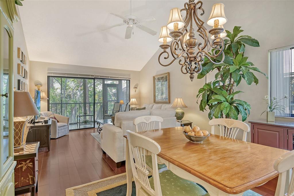 A dining area with a chandelier and wooden table opens into a living room with balcony — 1720 GLENHOUSE DRIVE UNIT GL430, SARASOTA, FL