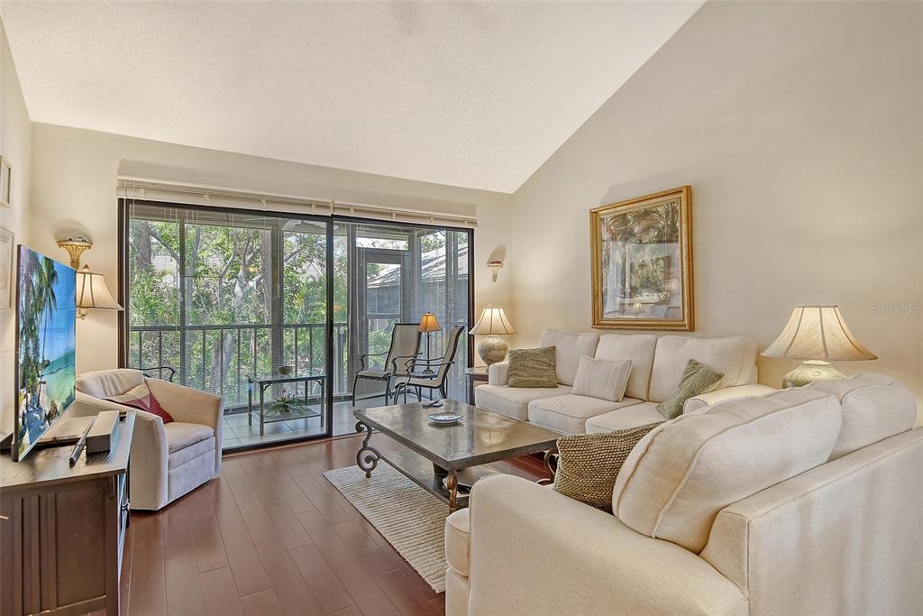 A living room features a vaulted ceiling, hardwood floors, a sofa, and a screened-in balcony — 1720 GLENHOUSE DRIVE UNIT GL430, SARASOTA, FL