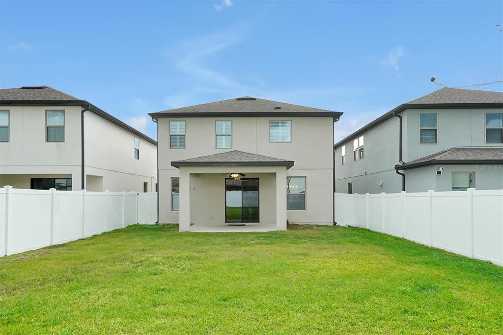 The rear exterior of a two-story house features a covered patio and a fenced yard — 9872 AUREA MOSS LANE, ORLANDO, FL