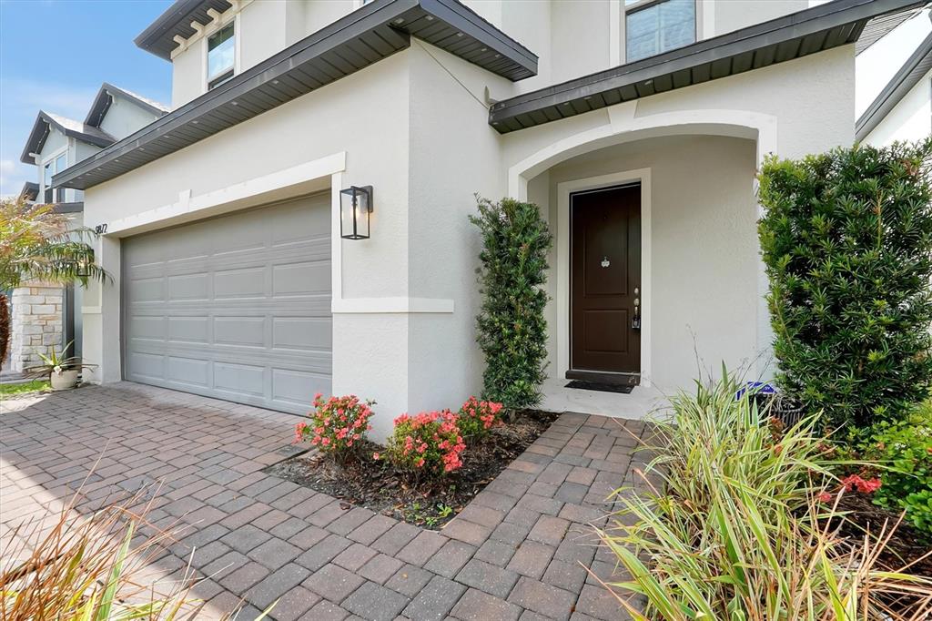The exterior of a house features a gray garage door, a brown front door, and landscaping — 9872 AUREA MOSS LANE, ORLANDO, FL