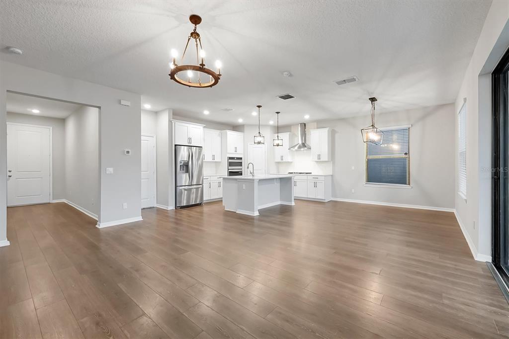 An open-concept kitchen features white cabinetry, a central island, and wood-look flooring — 9872 AUREA MOSS LANE, ORLANDO, FL