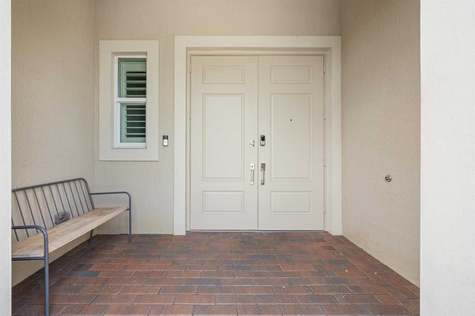 A beige double front door with a window and a metal bench on a patio — 5095 Beland Drive, Lake Worth FL 33467, LAKE WORTH, FL
