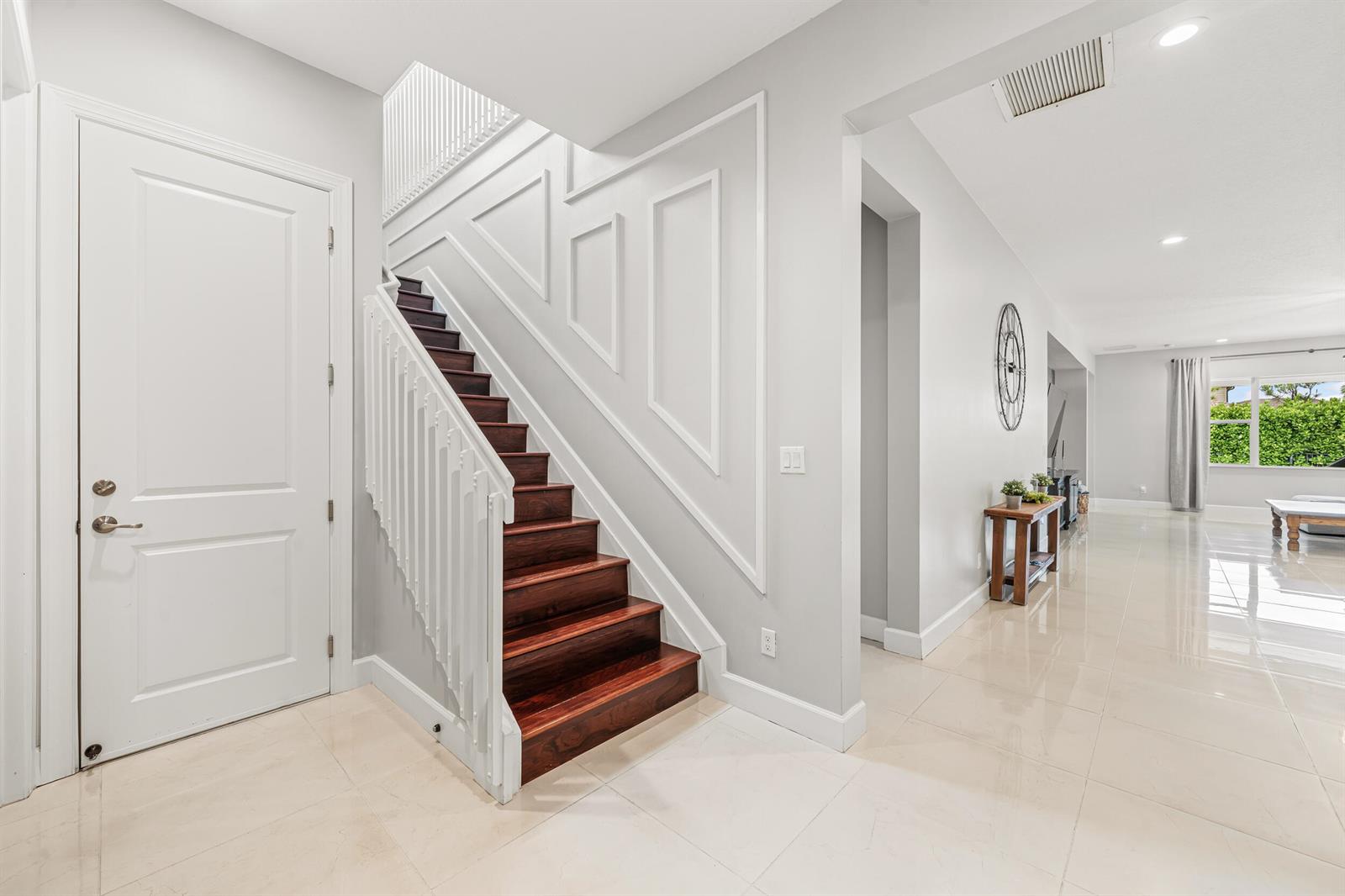 A bright entryway features a dark wood staircase with white railings and light tile flooring — 5095 Beland Drive, Lake Worth FL 33467, LAKE WORTH, FL
