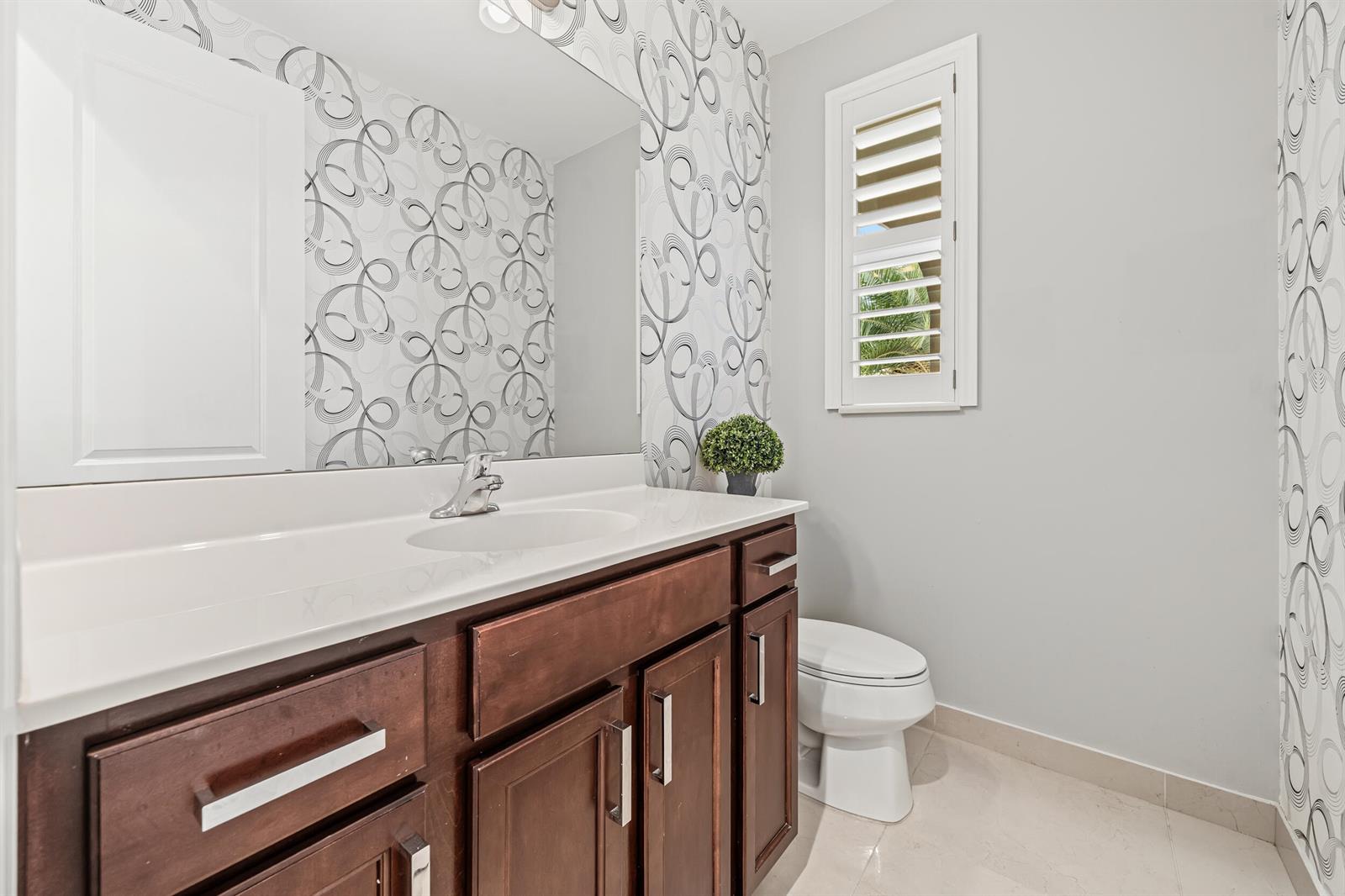 A bathroom features a dark wood vanity, a white countertop, and patterned wallpaper — 5095 Beland Drive, Lake Worth FL 33467, LAKE WORTH, FL