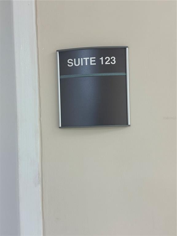 A dark gray sign with the text SUITE 123 is mounted on a beige wall — 5118 N 56TH STREET UNIT 123, TAMPA, FL