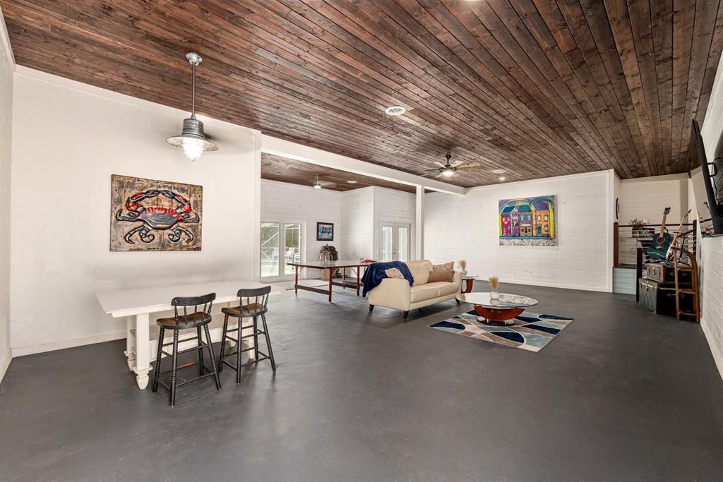 A spacious room with a wood-plank ceiling, gray concrete floors, and a casual seating area — 19451 SE 2ND STREET, WILLISTON, FL