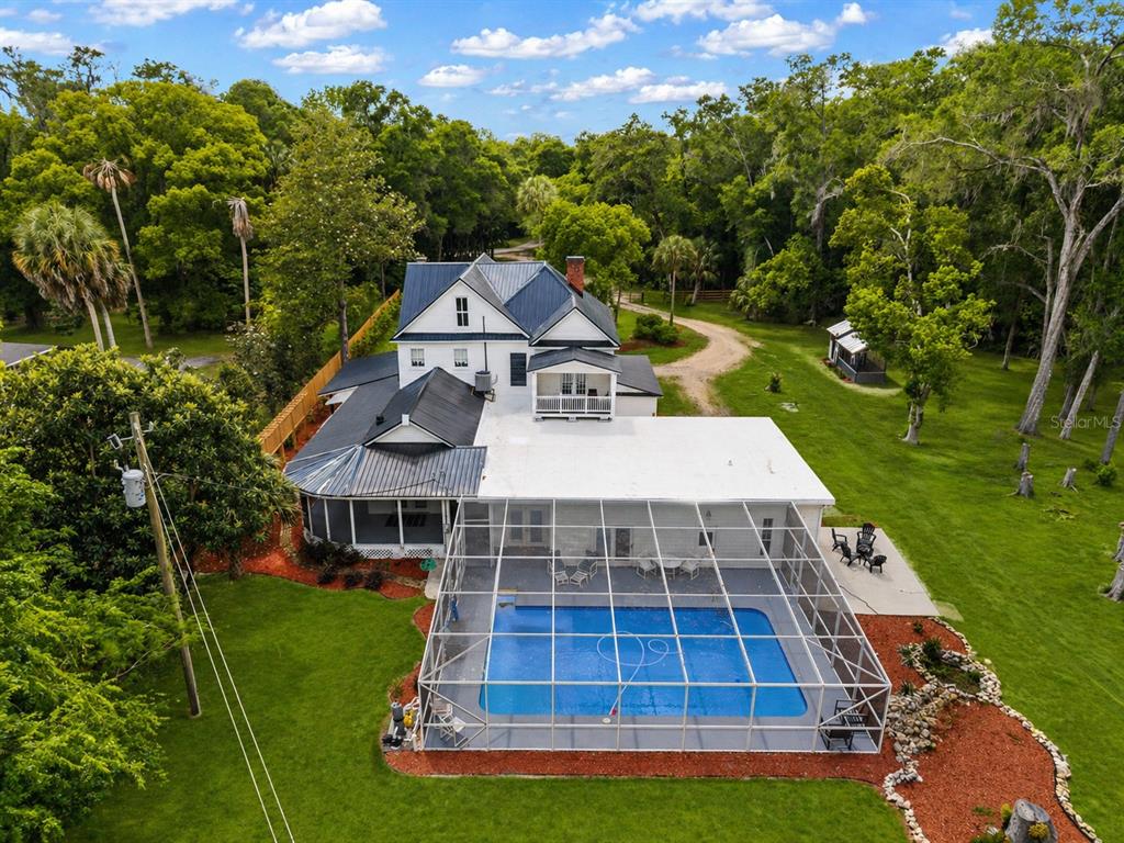 An aerial view of a white farmhouse with a screened-in pool and metal roof — 19451 SE 2ND STREET, WILLISTON, FL