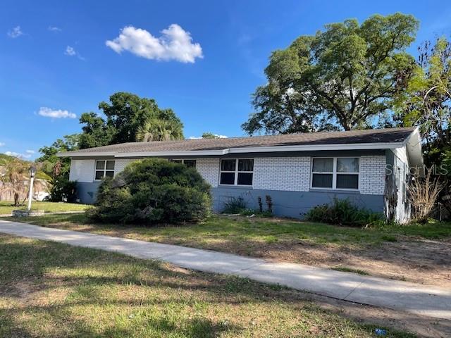 A single-story house with white brick siding and a gray roof sits behind a sidewalk — 6800 ANOKA DRIVE, ORLANDO, FL