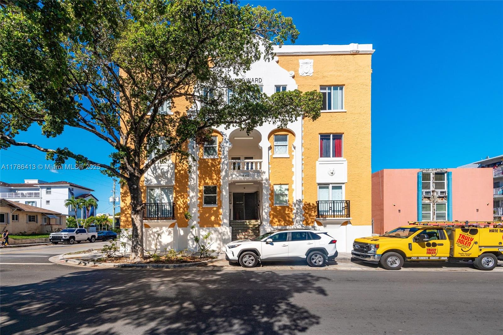 A yellow and white multi-story apartment building stands behind a large tree and parked cars — 440 SW 5th Ave, Miami FL 33130, MIAMI, FL