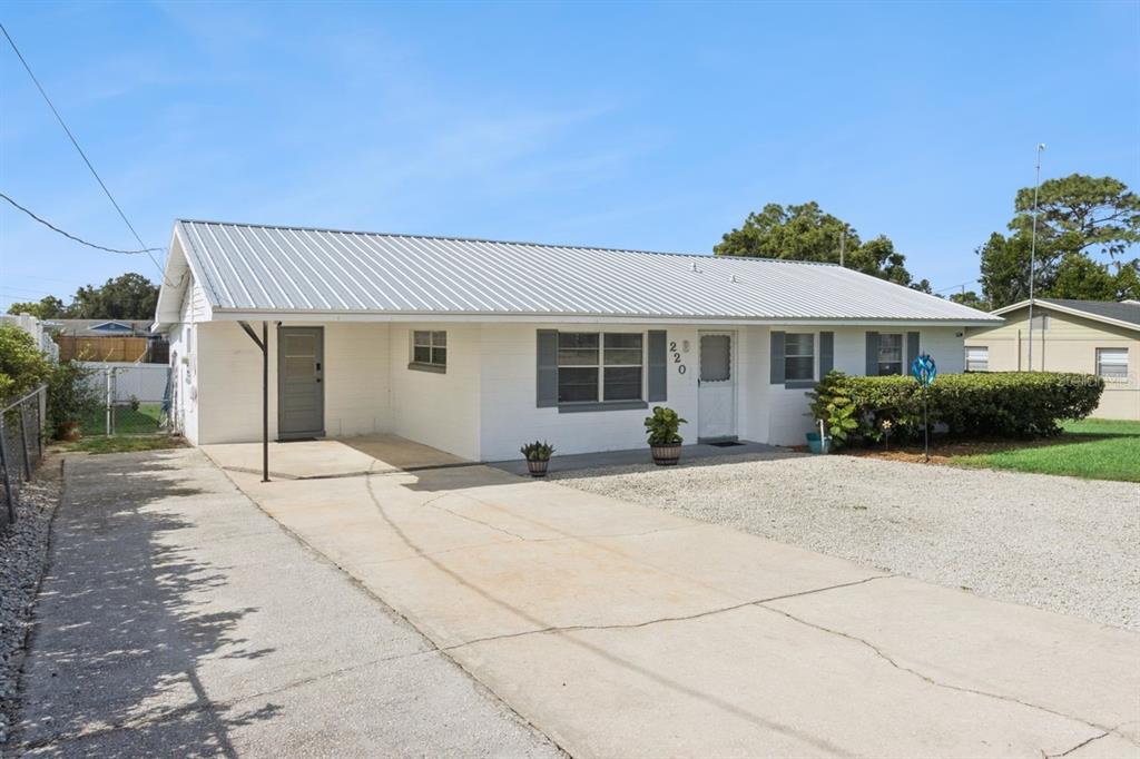 A single-story white house with a metal roof, concrete driveway, and a covered entryway — 220 ALDO DRIVE, BABSON PARK, FL
