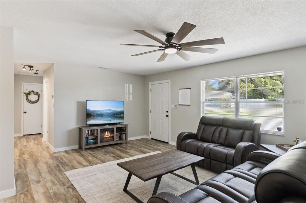 A living room features wood-look flooring, a ceiling fan, a television console, and leather furniture — 220 ALDO DRIVE, BABSON PARK, FL