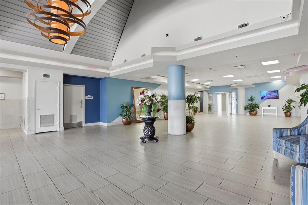 A spacious lobby features light-colored tile flooring, a vaulted ceiling, and blue accent walls — 2700 N ATLANTIC AVENUE UNIT 407, DAYTONA BEACH, FL